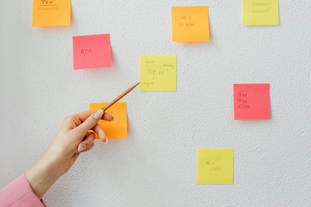 Hand pointing at colorful sticky notes with business concepts on a wall.